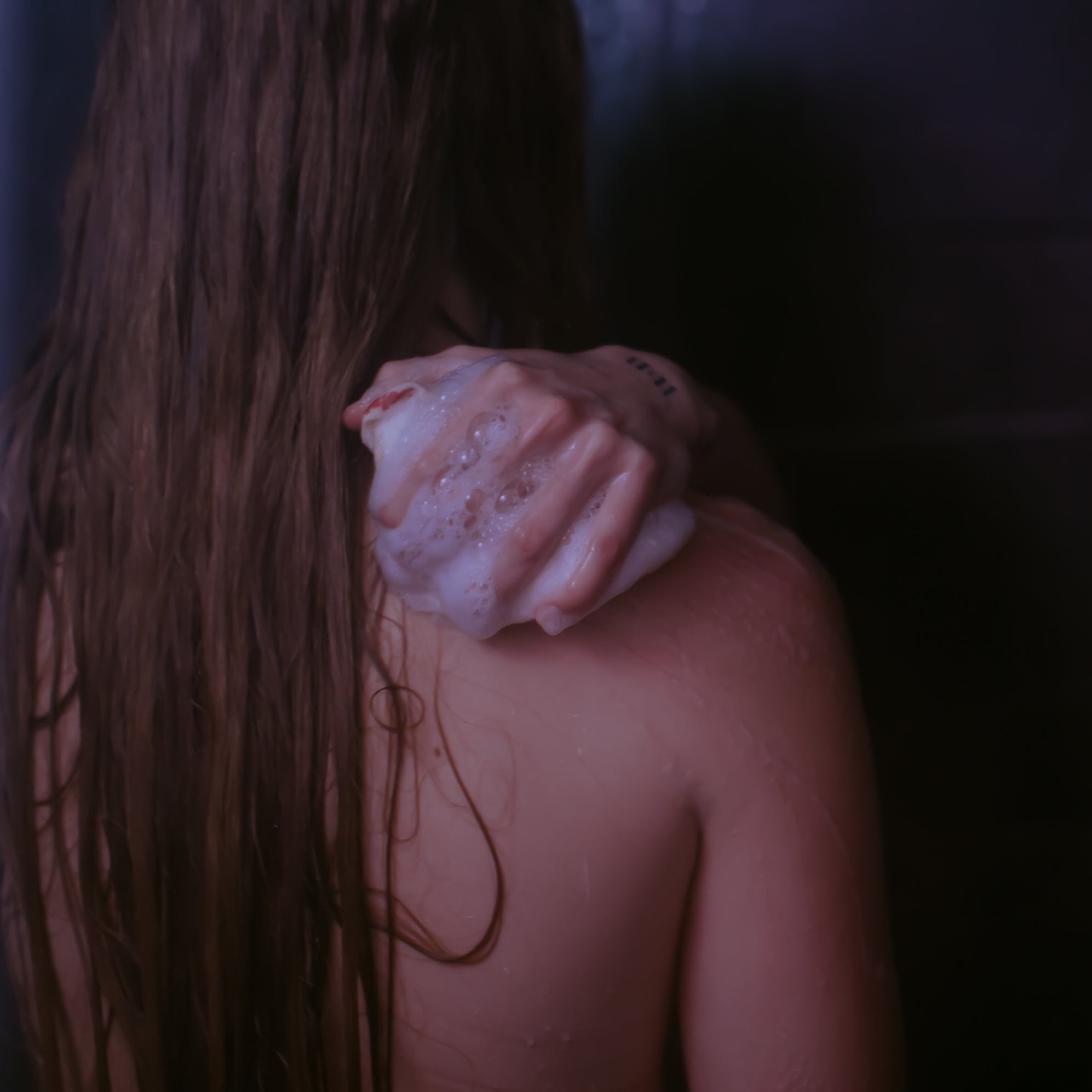 Person with long hair holding a Floofah shower loofah against a dark background
